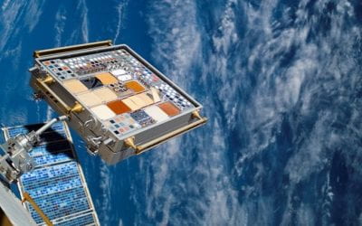 Satellite hardware mounted on a space station platform, with Earth’s blue surface and clouds visible in the background.