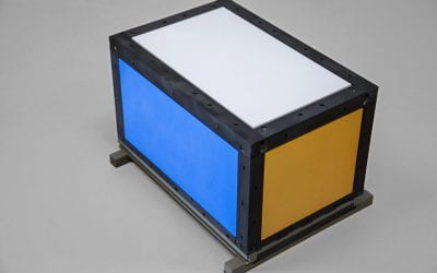 Rectangular CubeSat satellite model with a black frame and colored side panels (blue and yellow), shown resting on a display stand.