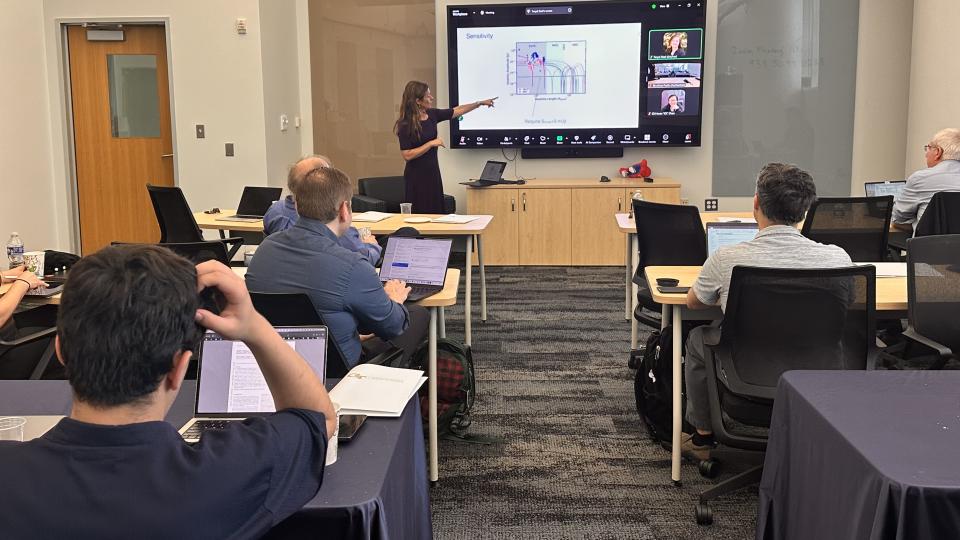 Image of classroom with woman pointing at a screen with full class in front of her.
